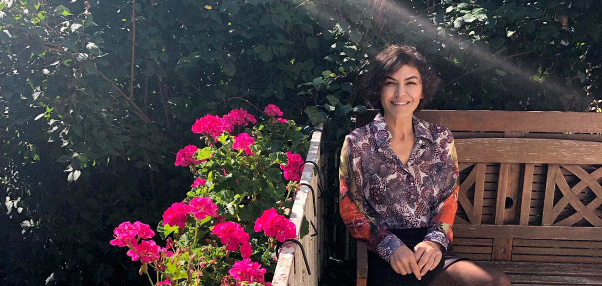 Dr. Rezan Cezan, pembe sardunyaların yanında ahşap bir bankta oturuyor